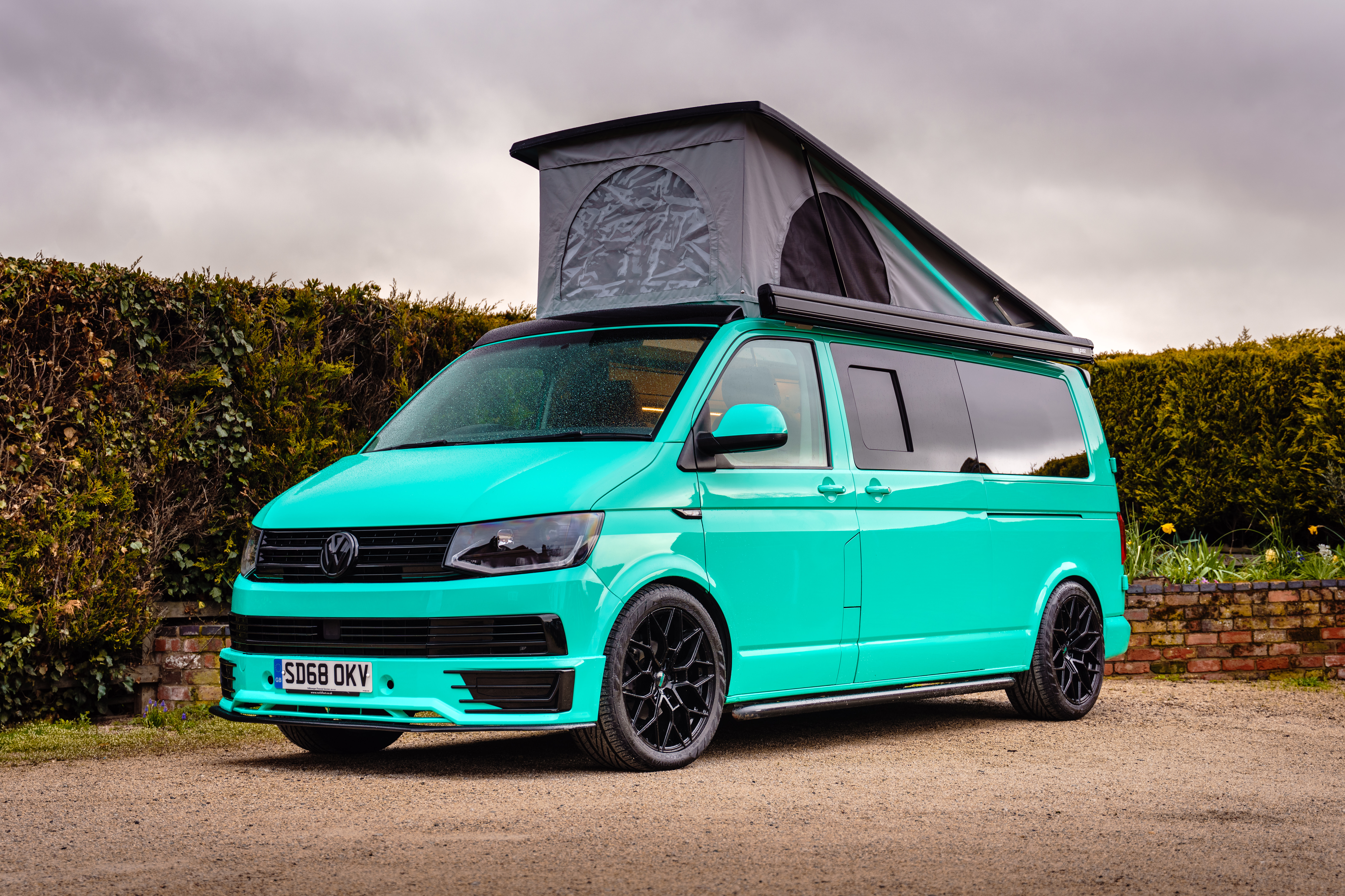 A turquoise campervan parked outdoors with its pop-top roof extended, demonstrating the design, build quality, and added height benefits to consider before investing in a pop-top roof for your van.